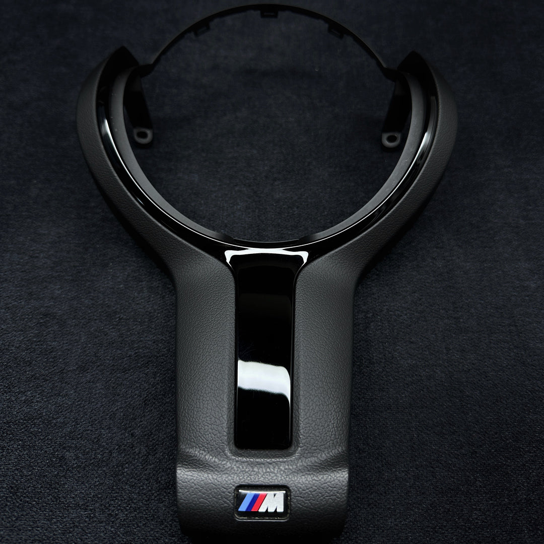 A black steering wheel trim with the BMW M brand logo in the center.