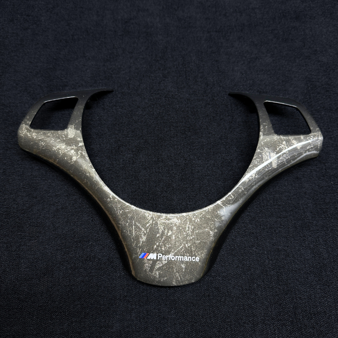 A forged carbon style steering wheel trim with a textured finish, branded with Performance BMW