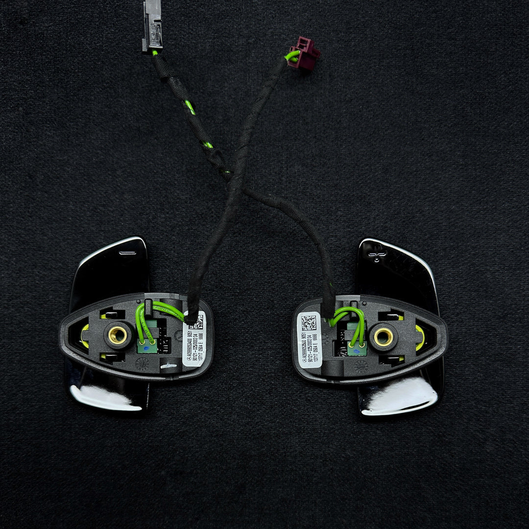 A pair of black Mercedes-Benz piano black shift paddles with a carbon fiber-like texture