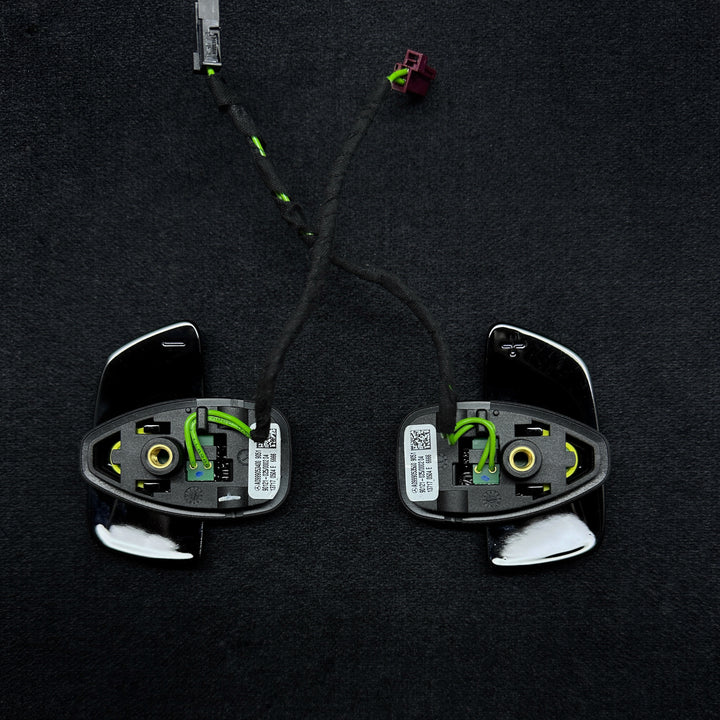 A pair of black Mercedes-Benz piano black shift paddles with a carbon fiber-like texture