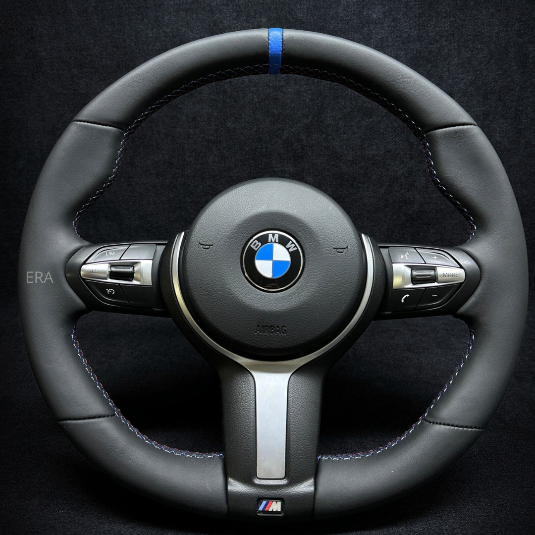 A black NAPPA leather BMW F-Series steering wheel with a blue stripe and M-branding.