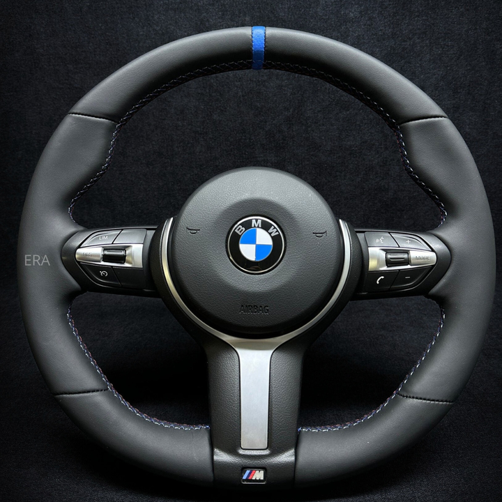 A black NAPPA leather BMW F-Series steering wheel with a blue stripe and M-branding.