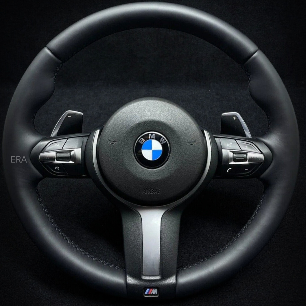 A black leather BMW F-Series steering wheel with stitching and shift paddles.