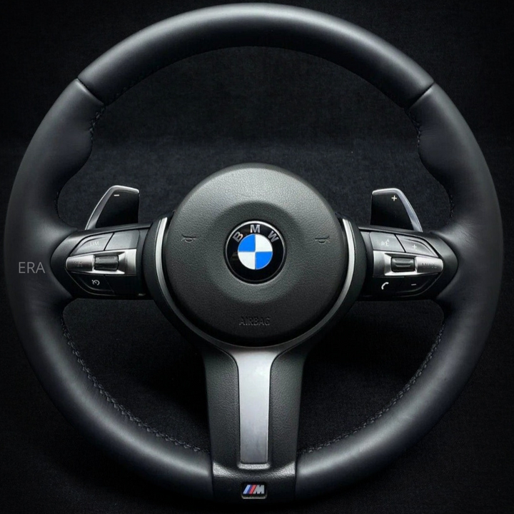 A black leather BMW F-Series steering wheel with stitching and shift paddles.